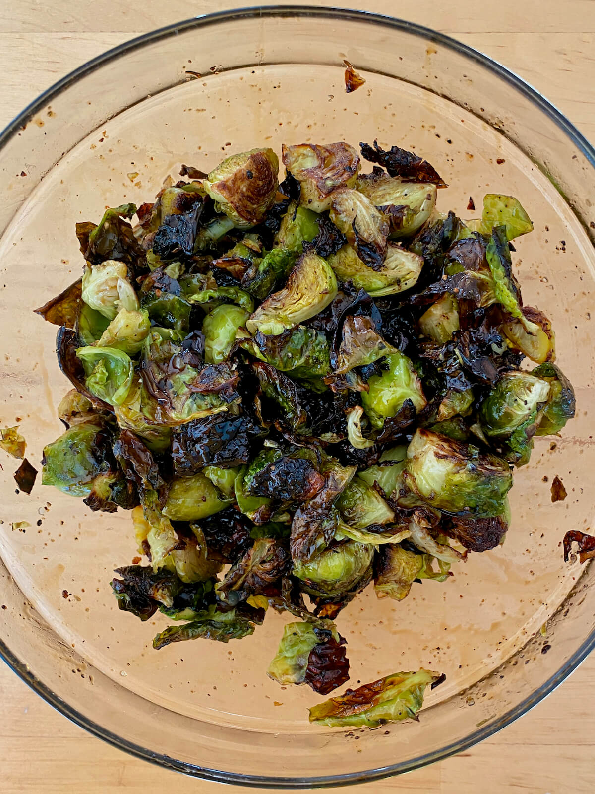 Roasted brussels sprouts tossed with maple balsamic glaze in a glass mixing bowl.