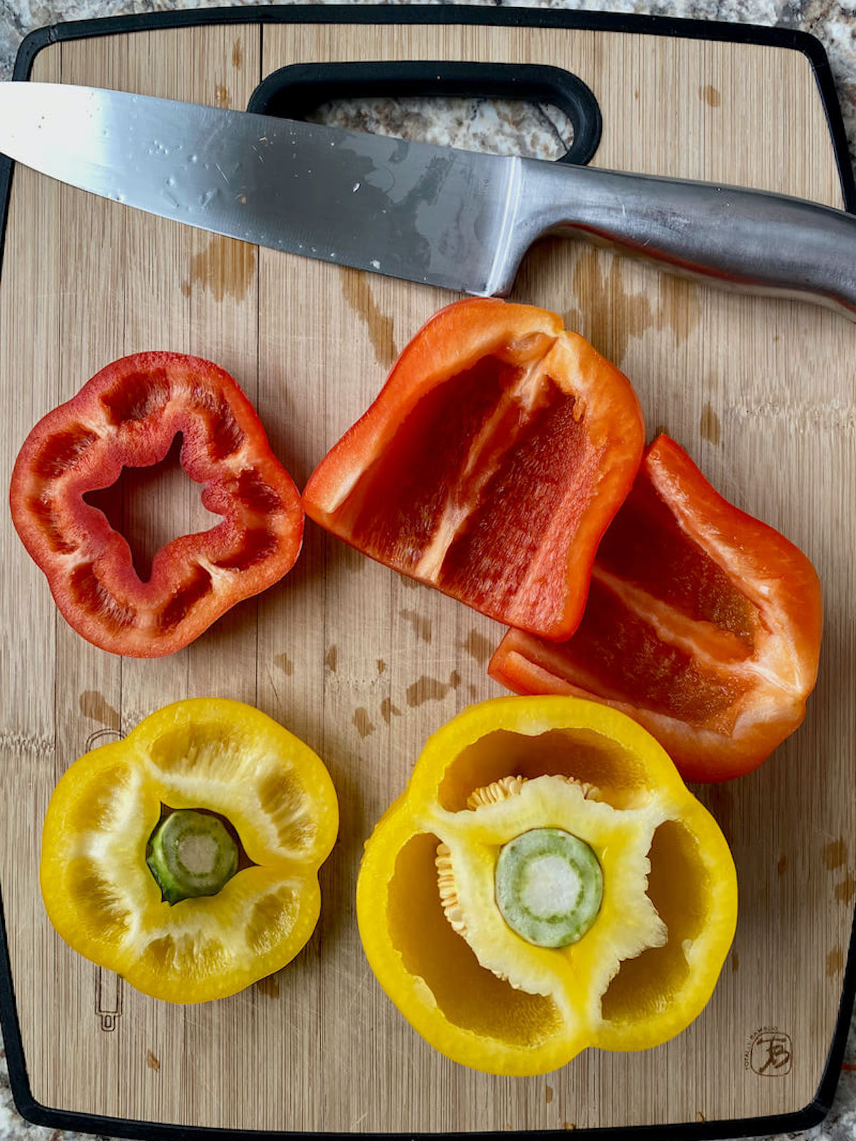 Raw bell peppers being cut on a bamboo cutting board.