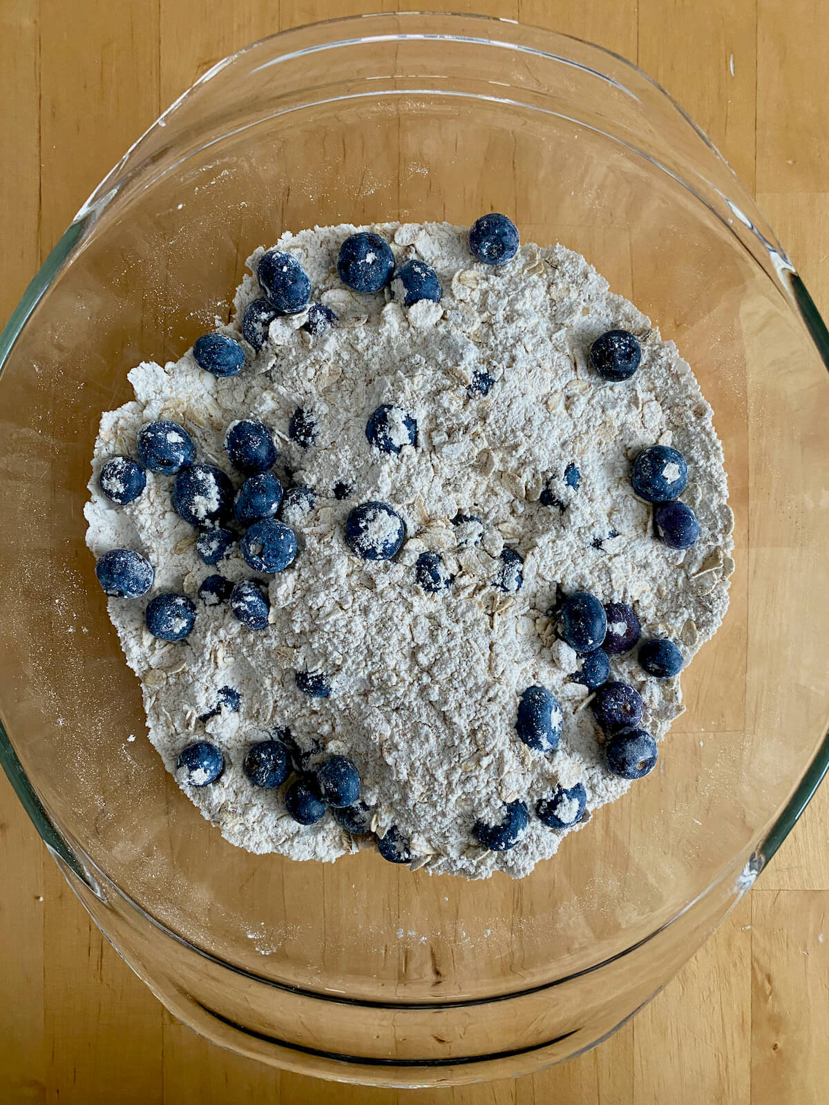 The dry ingredients and fresh blueberries mixed together in a large glass mixing bowl.