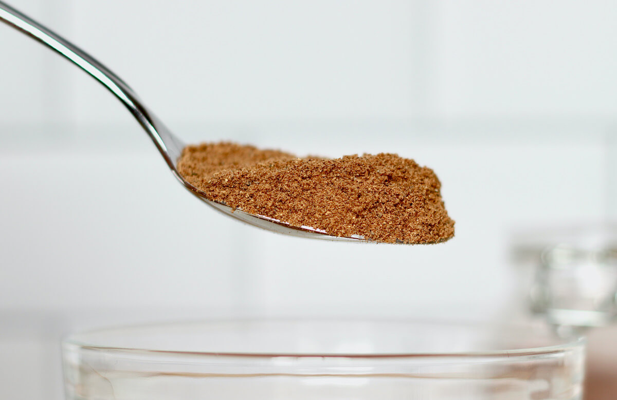 A spoonful of chai spice blend being held above a small glass mixing bowl.