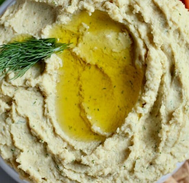 A bowl of lemon dill hummus garnished with olive oil and dill sprigs.