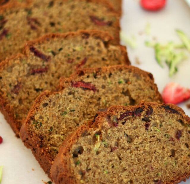 Slices of strawberry zucchini bread laid out across a piece of parchment paper.