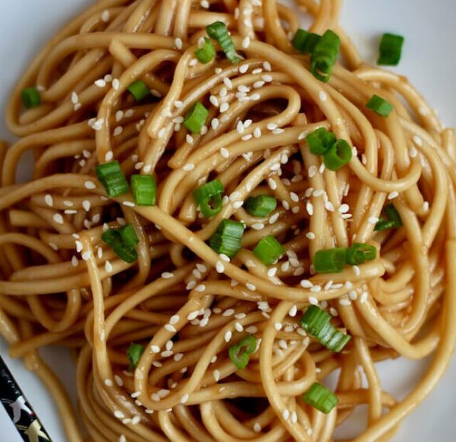 A plate of teriyaki udon noodles garnished with sesame seeds and green onions.