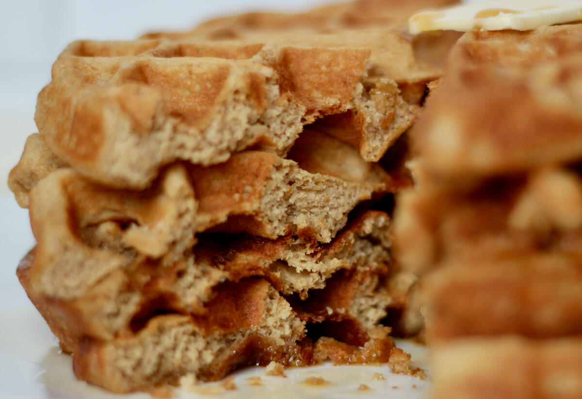 A stack of oat flour waffles with a section cut out to show the texture of the inside.