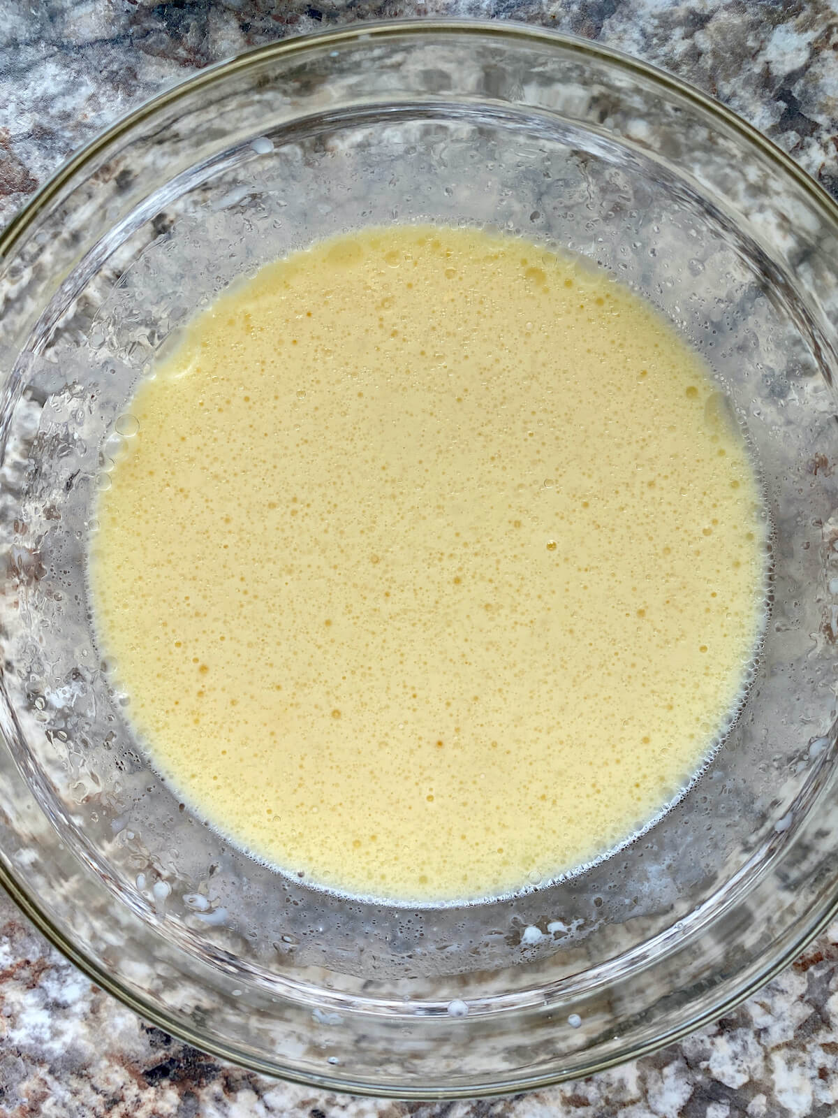 A glass bowl filled with a mix of buttermilk, eggs, vanilla extract, and canola oil.