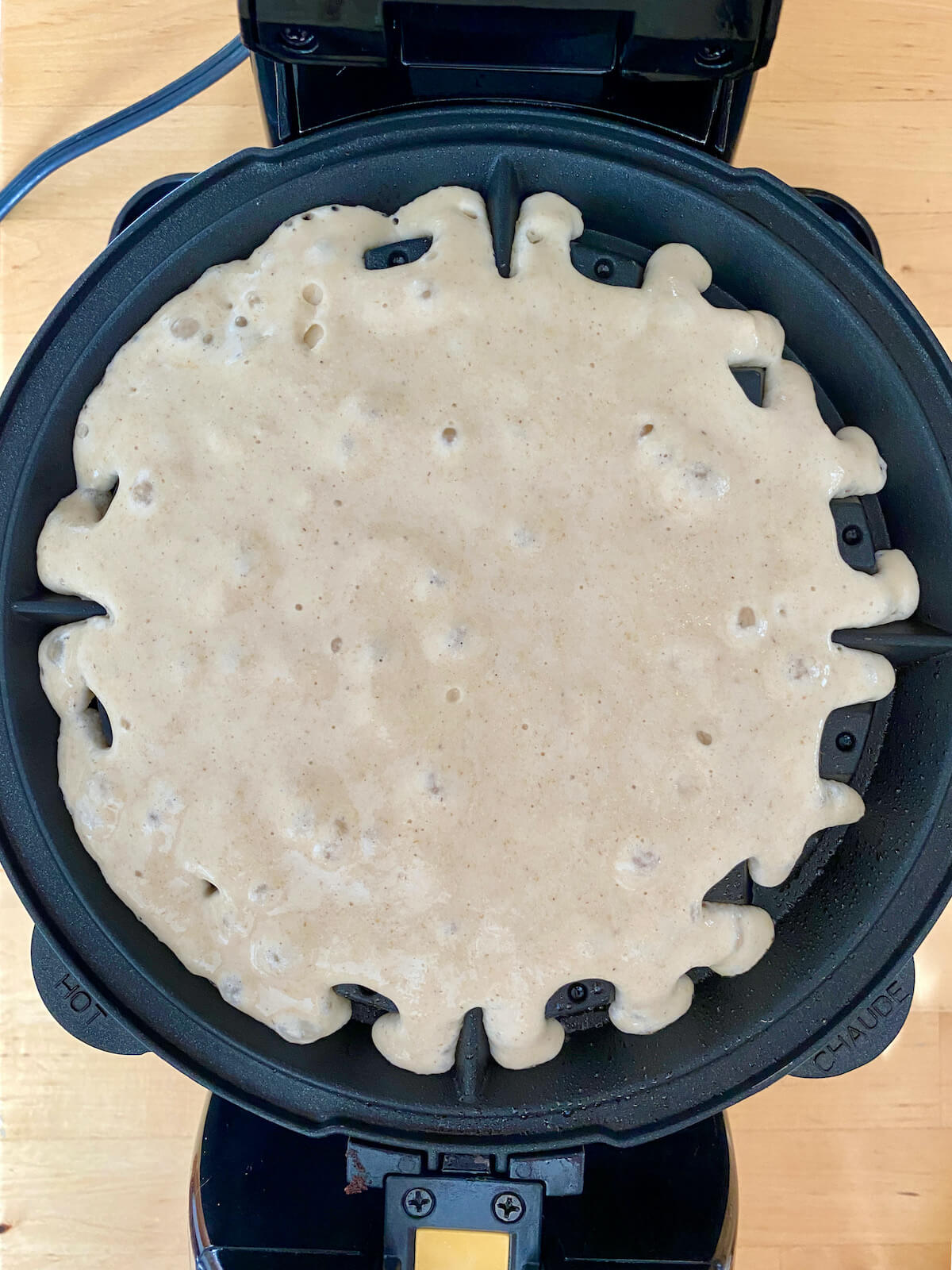 An oat flour waffle cooking in a waffle iron.