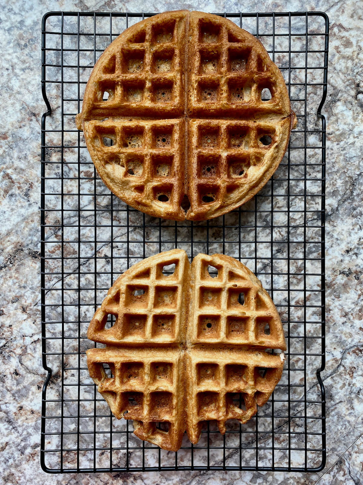 Two finished oat flour waffles on a cooling rack.