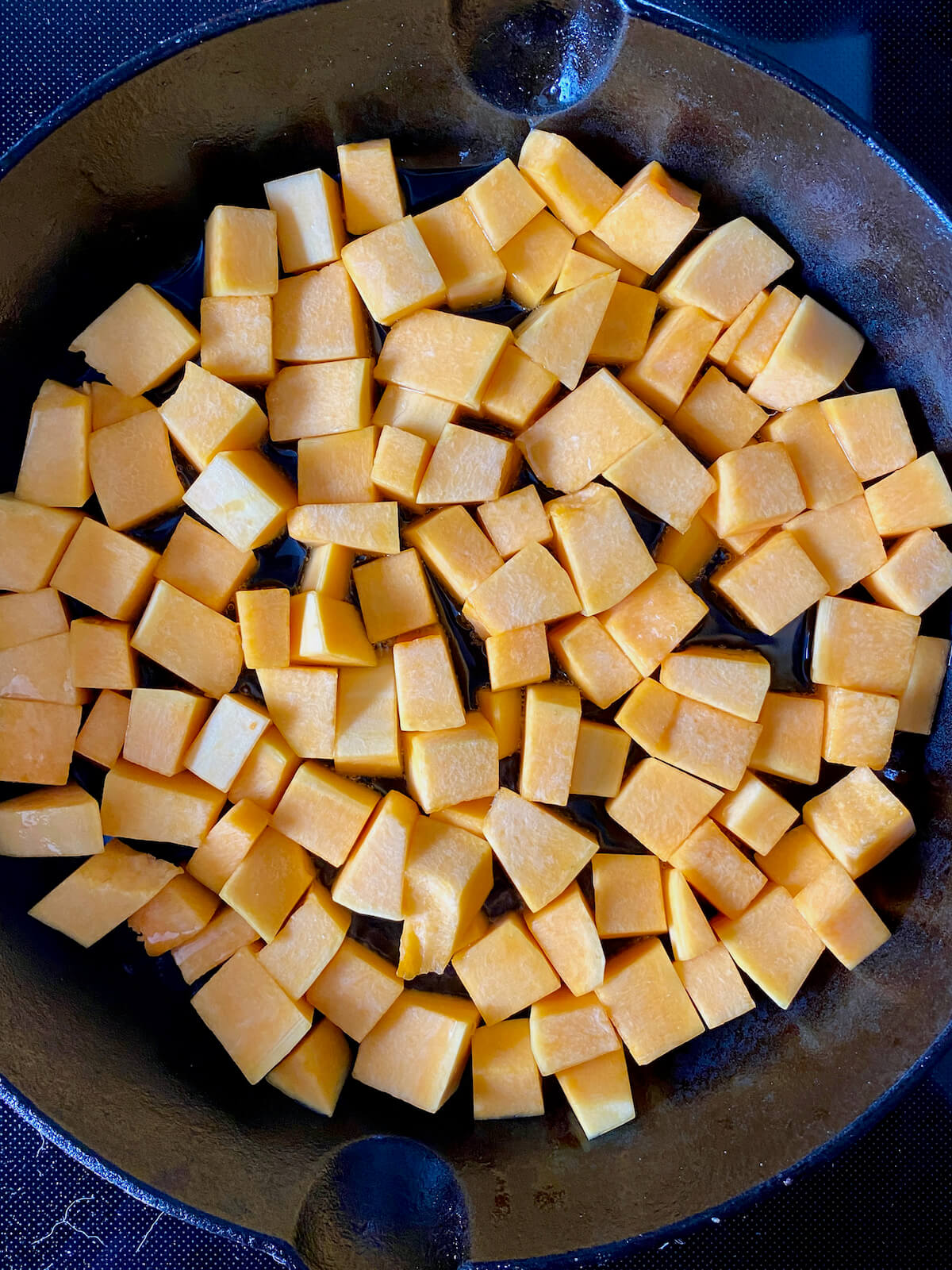 Raw, cubed butternut squash in a cast iron skillet.