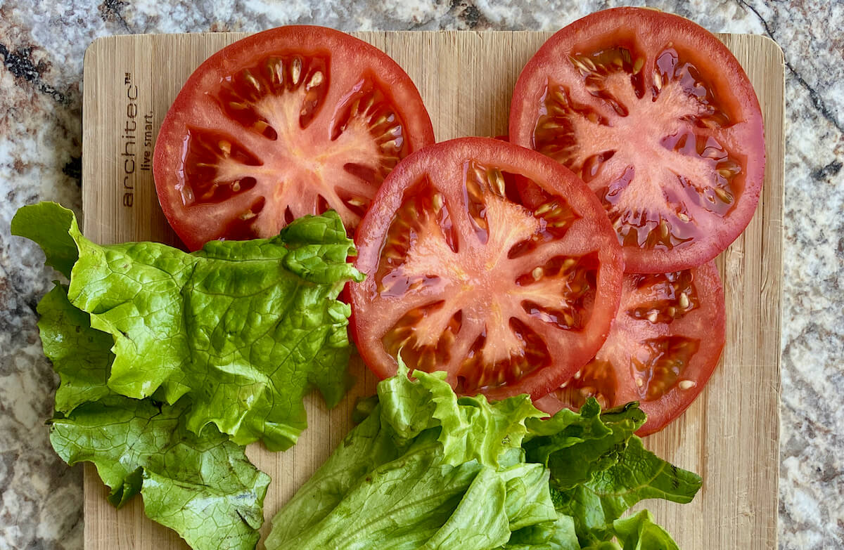 Slices of tomato and lettuce on a cutting board.