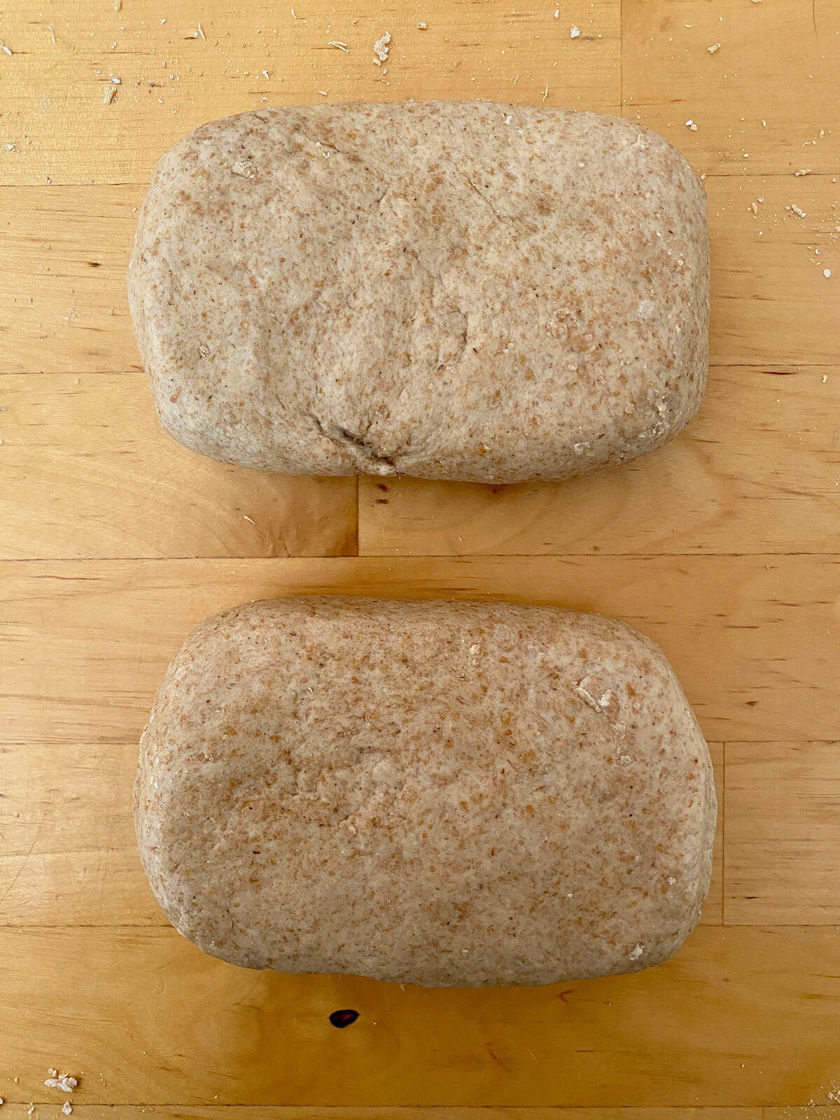 Two pieces of sourdough cracker dough shaped into rectangles on a butcher block countertop.
