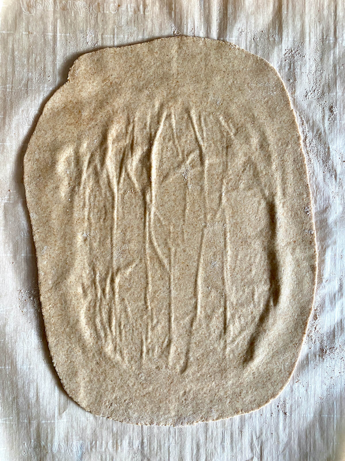 The sourdough cracker dough rolled out onto a piece of parchment paper.