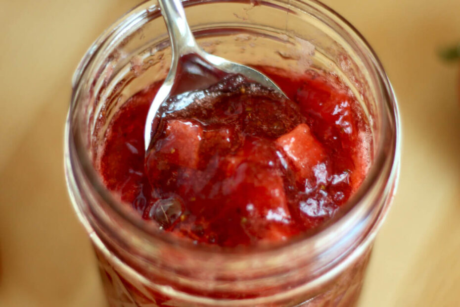 An open jar of strawberry apple jam with a spoon scooping some out of the top.