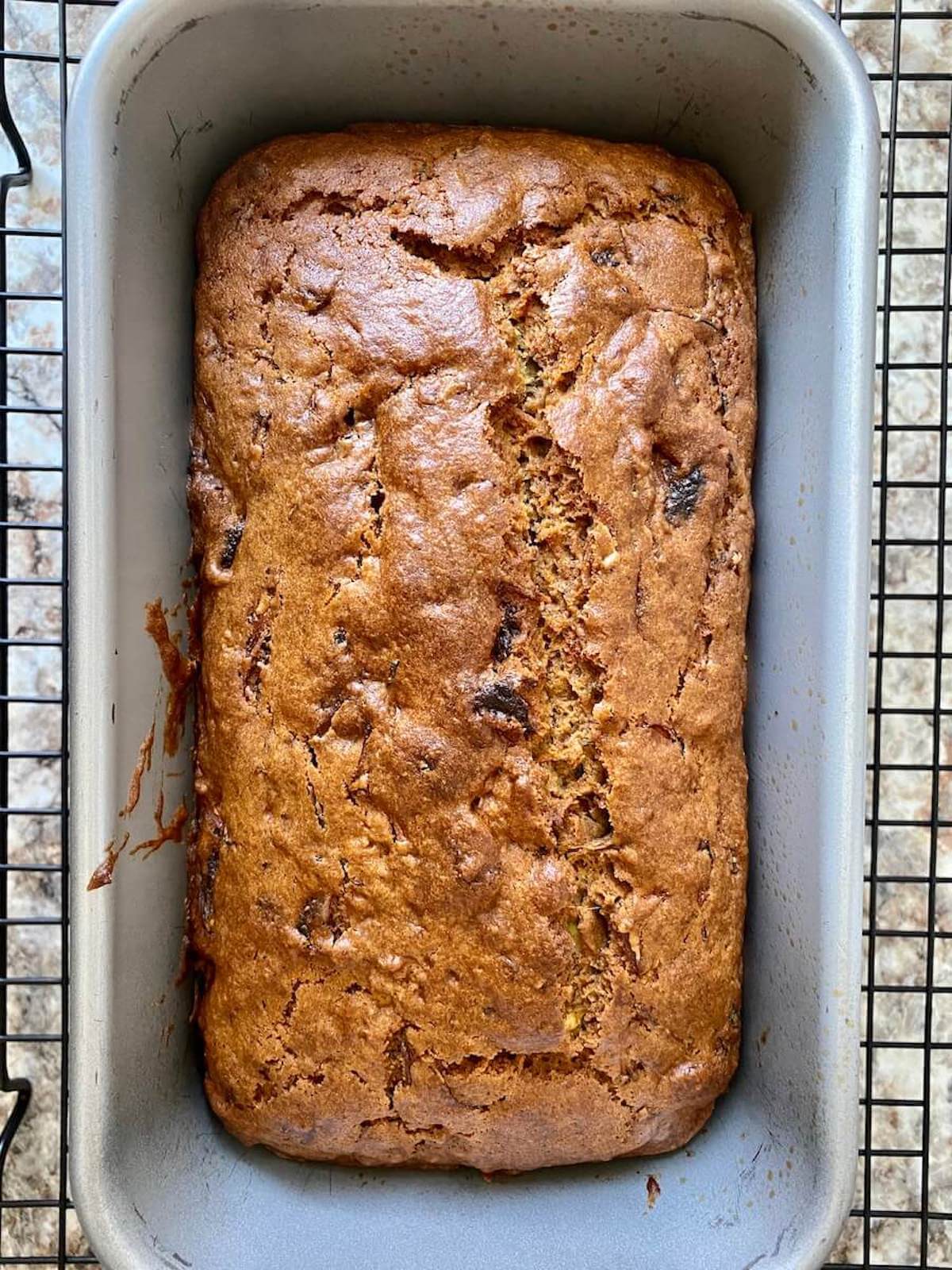 A loaf of strawberry zucchini bread still in the loaf pan on a cooling rack.