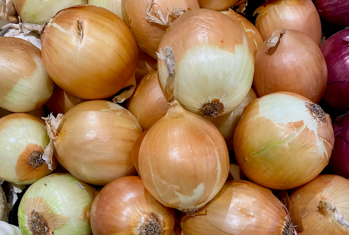 A pile of yellow onions on a grocery store shelf.