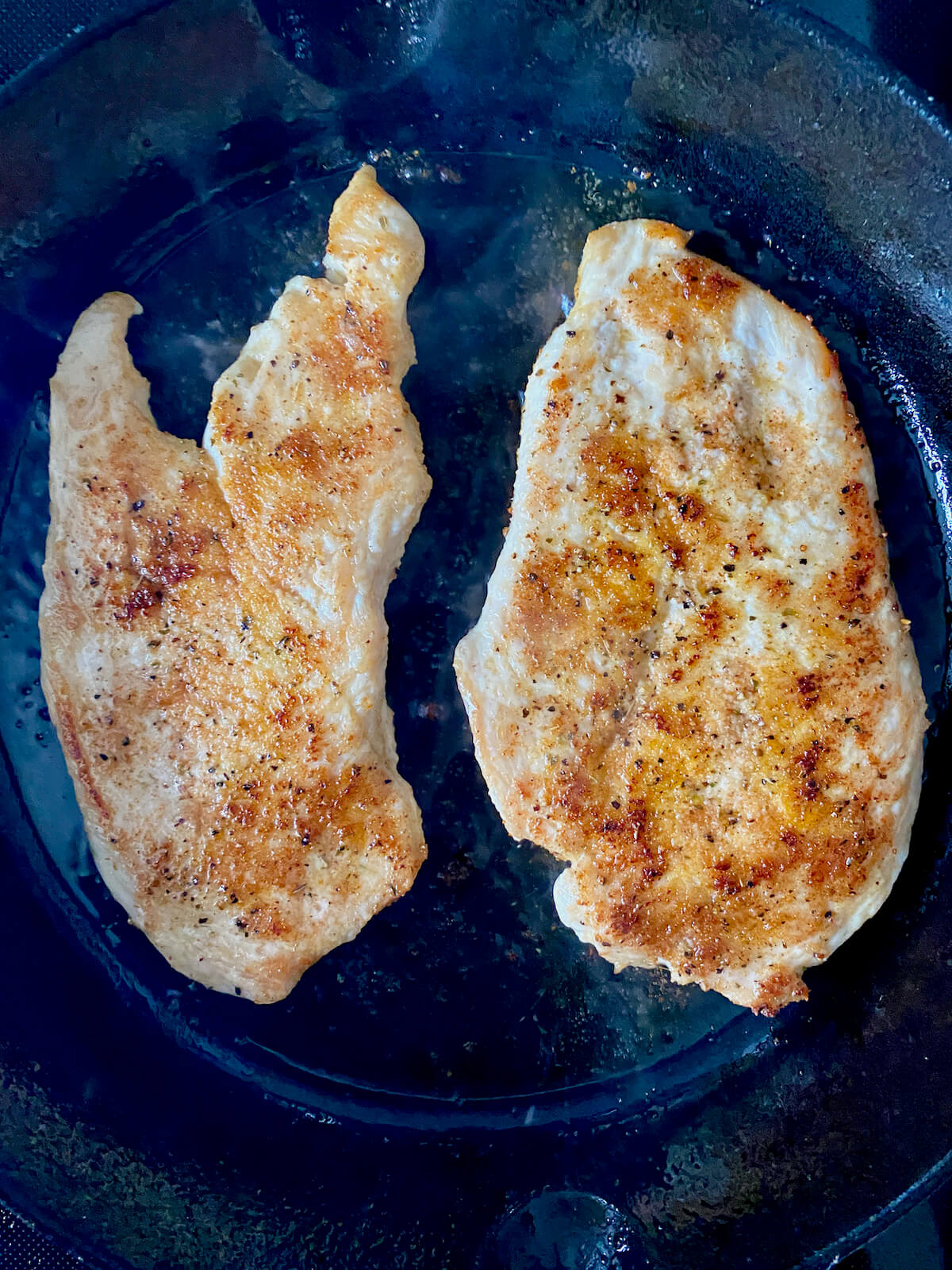 Two chicken breasts after being flipped in a cast iron skillet.