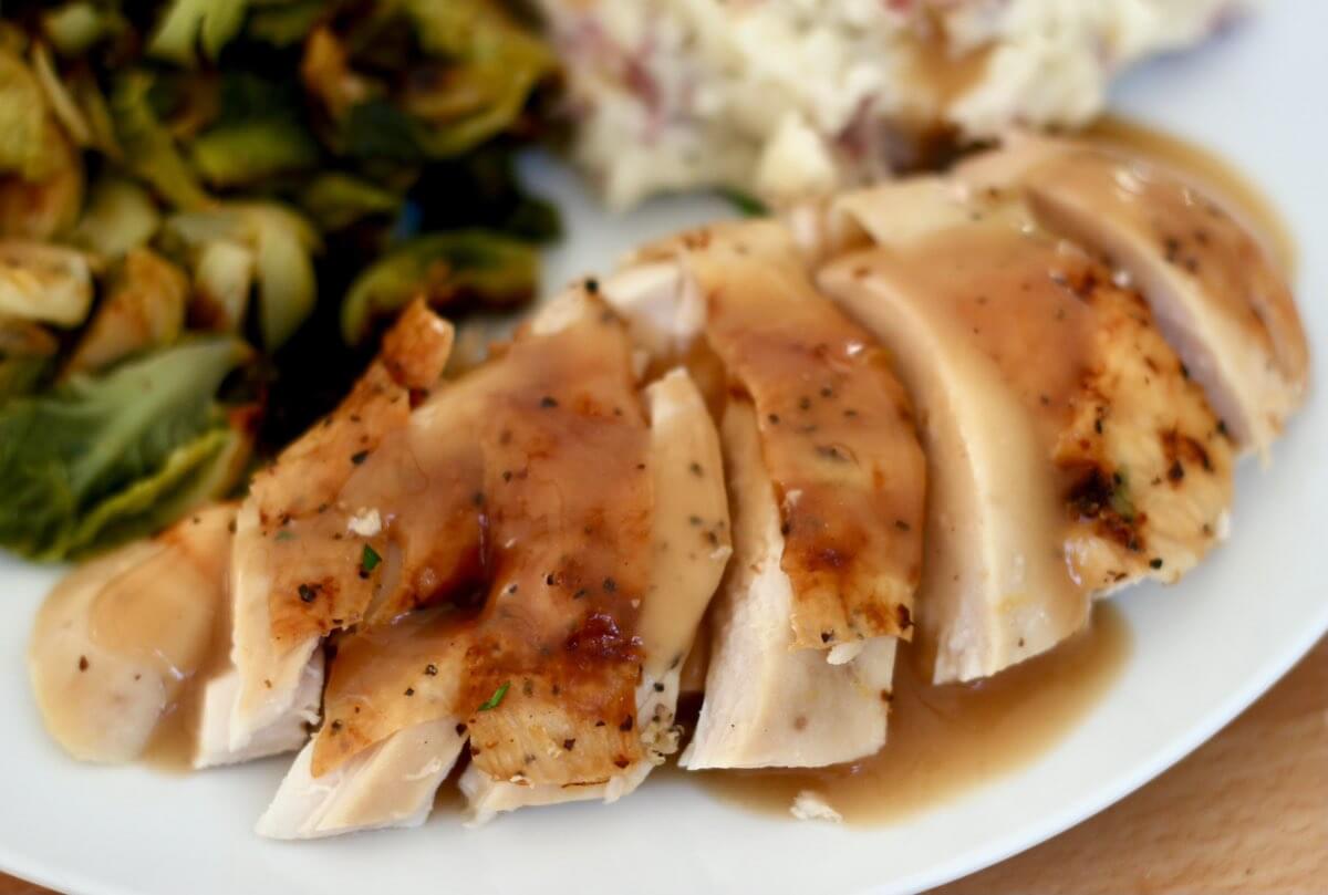 Sliced dry brined chicken on a dinner plate with gravy, mashed potatoes, and Brussels sprouts.