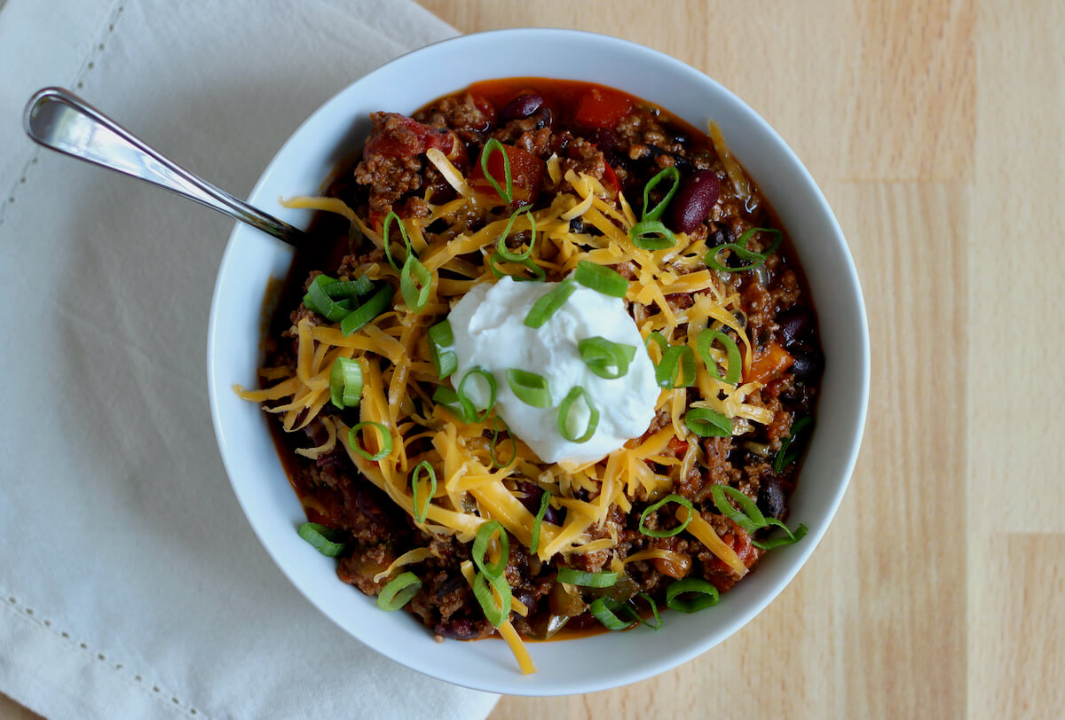 A bowl of Dutch oven chili topped with cheddar cheese, sour cream, and scallions.