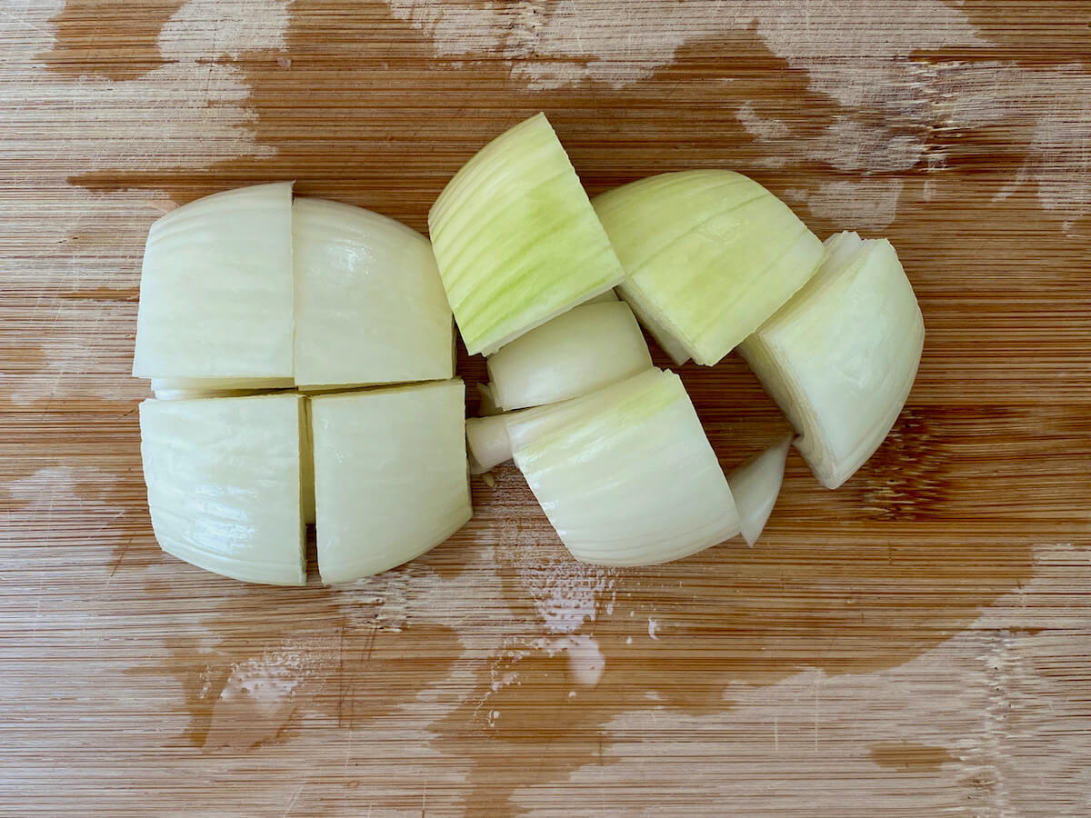 An onion cut into large chunks on a bamboo cutting board.