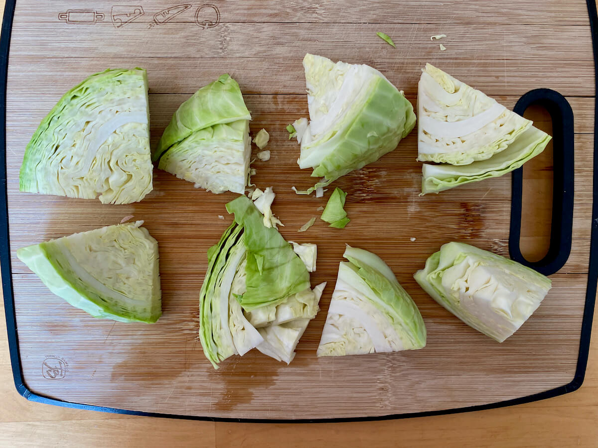 Green cabbage cut into large chunks on a bamboo cutting board.