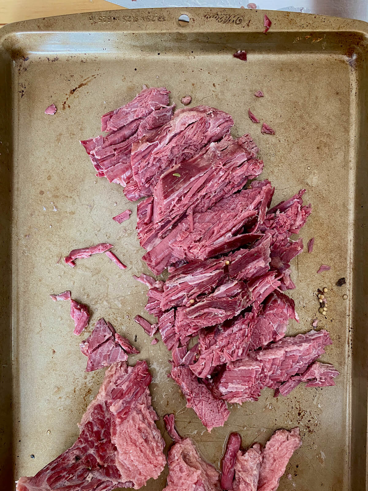 Sliced corned beef on a rimmed baking sheet.