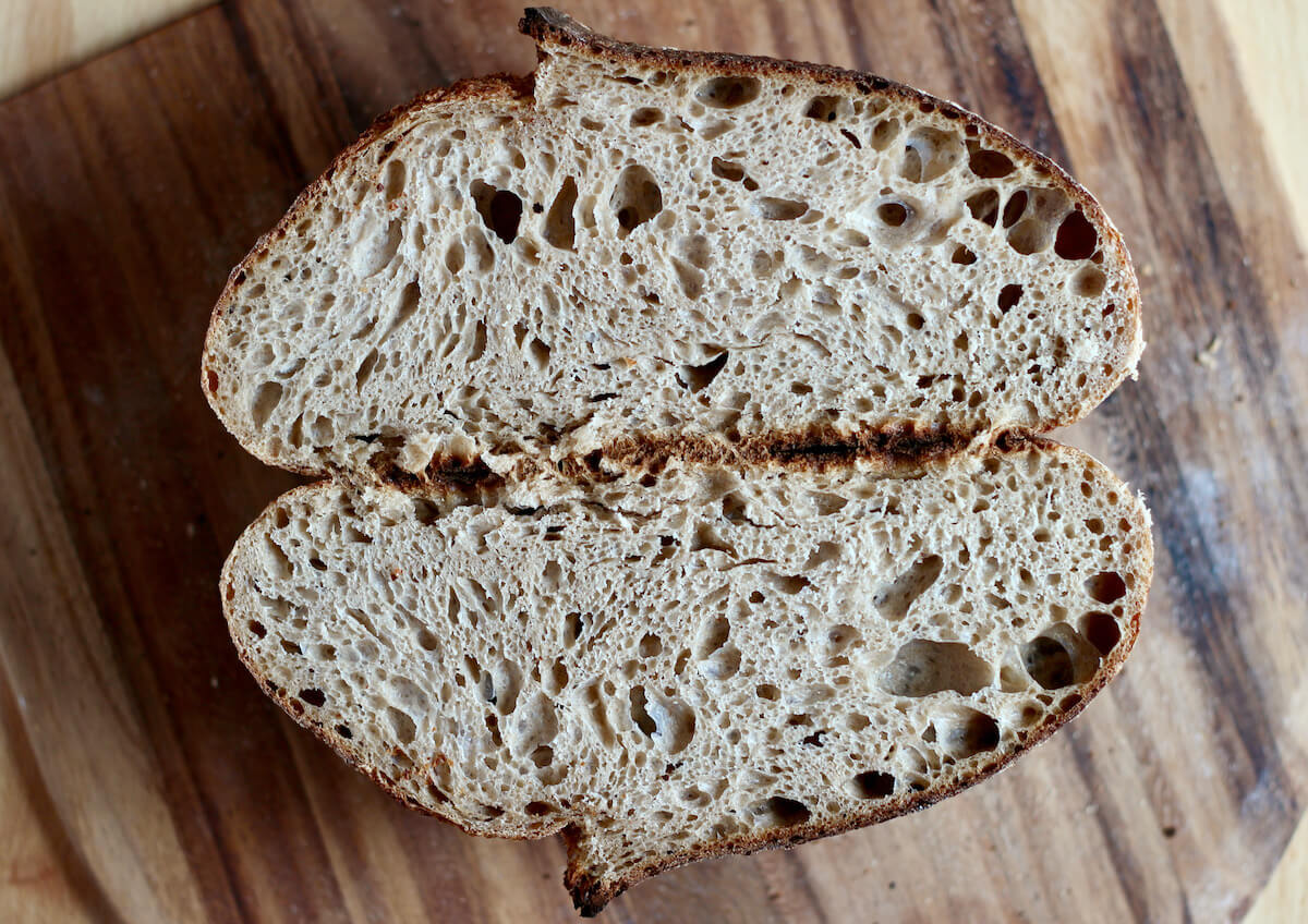 A loaf of Dutch oven sourdough bread cut in half on a wooden bread peel.