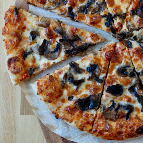 Mushroom pizza cut into 8 slices on a piece of parchment paper.