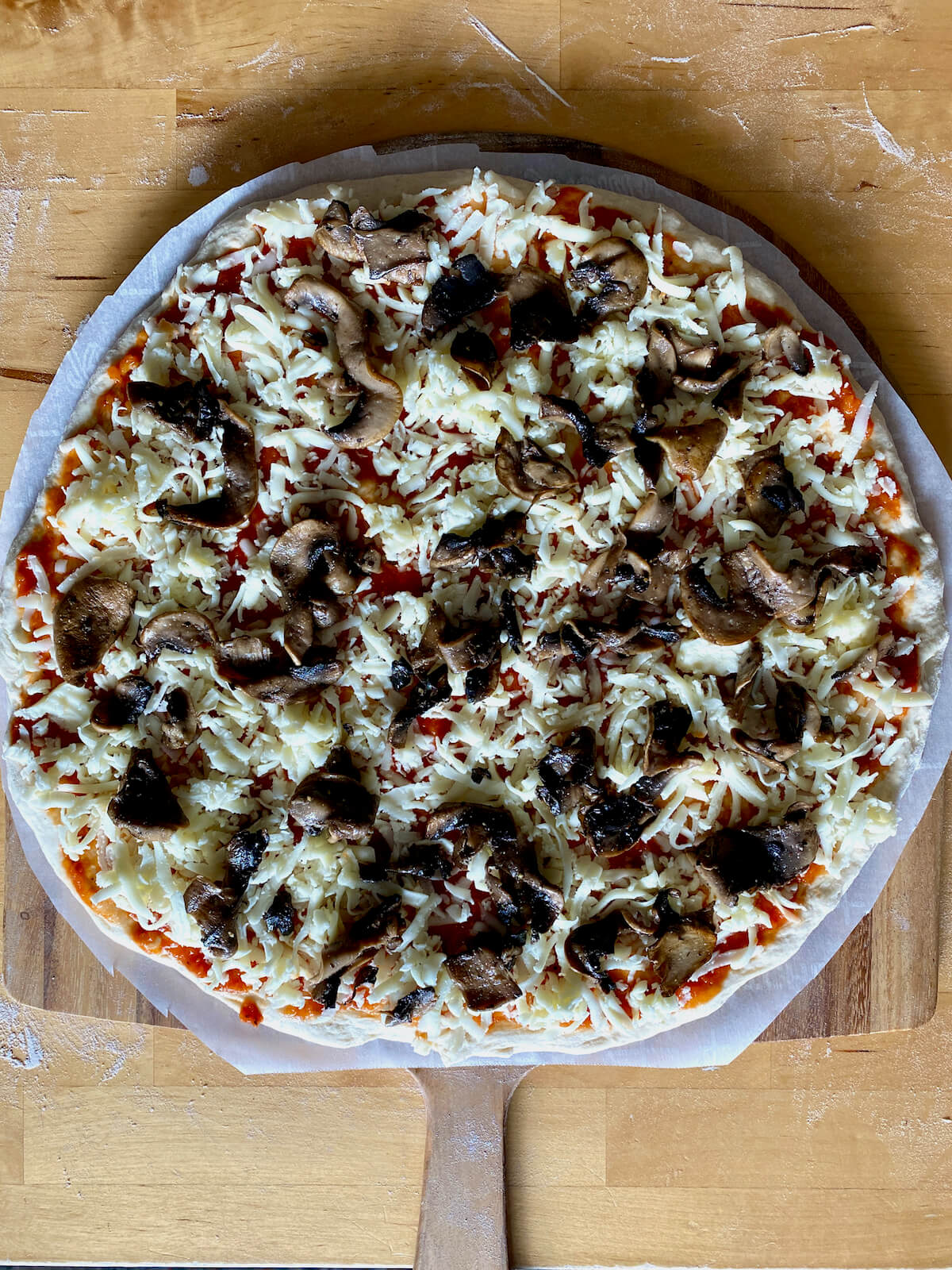 An assembled mushroom pizza on a pizza peel ready to be baked.