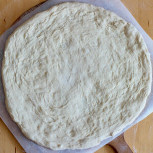 Sourdough discard pizza dough stretched out on a pizza peel.