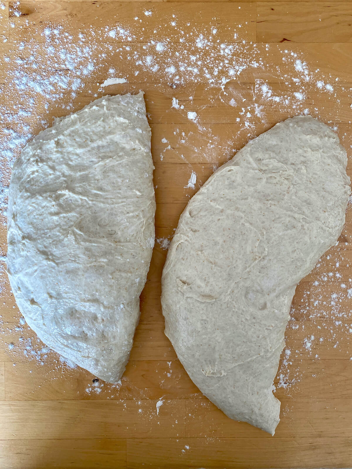 The pizza dough divided into two pieces on a countertop.