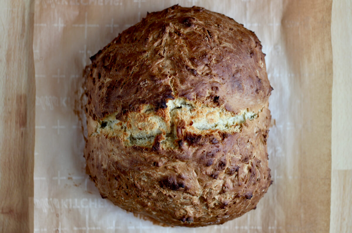 A loaf of sourdough Irish soda bread on a sheet of parchment paper.