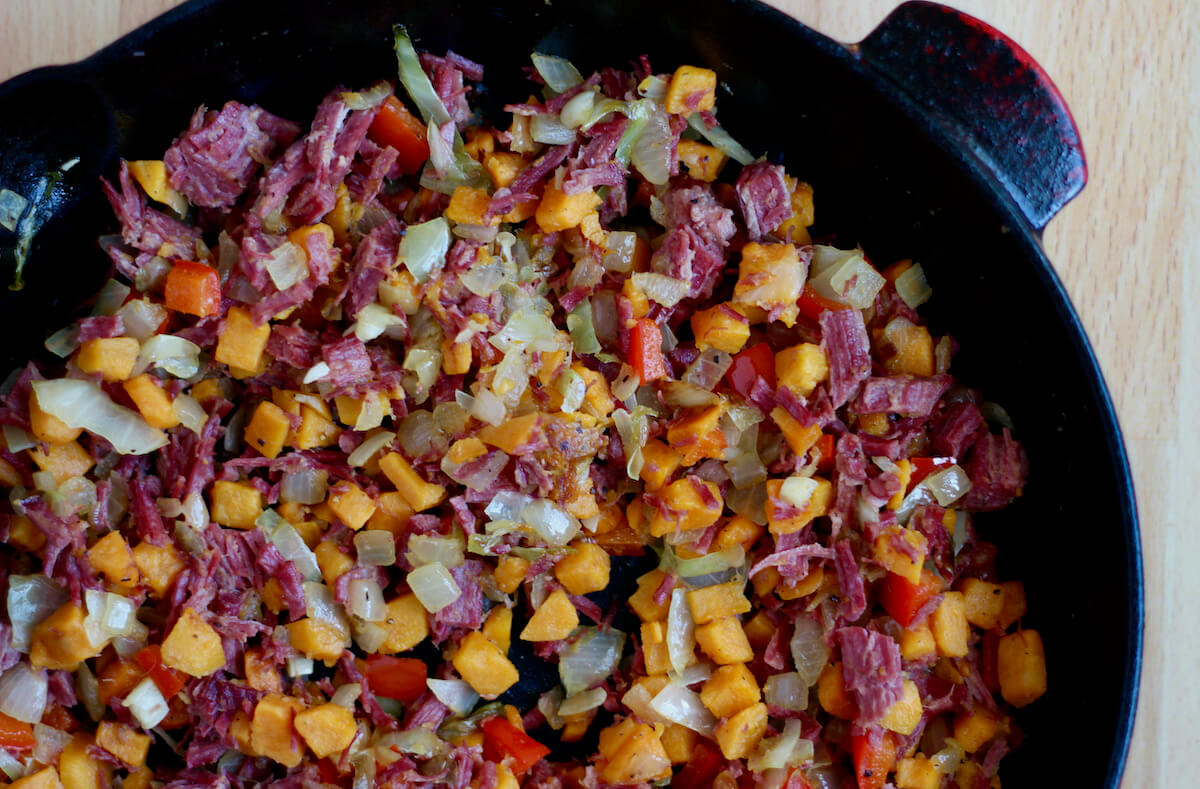A cast iron skillet filled with sweet potato corned beef hash.