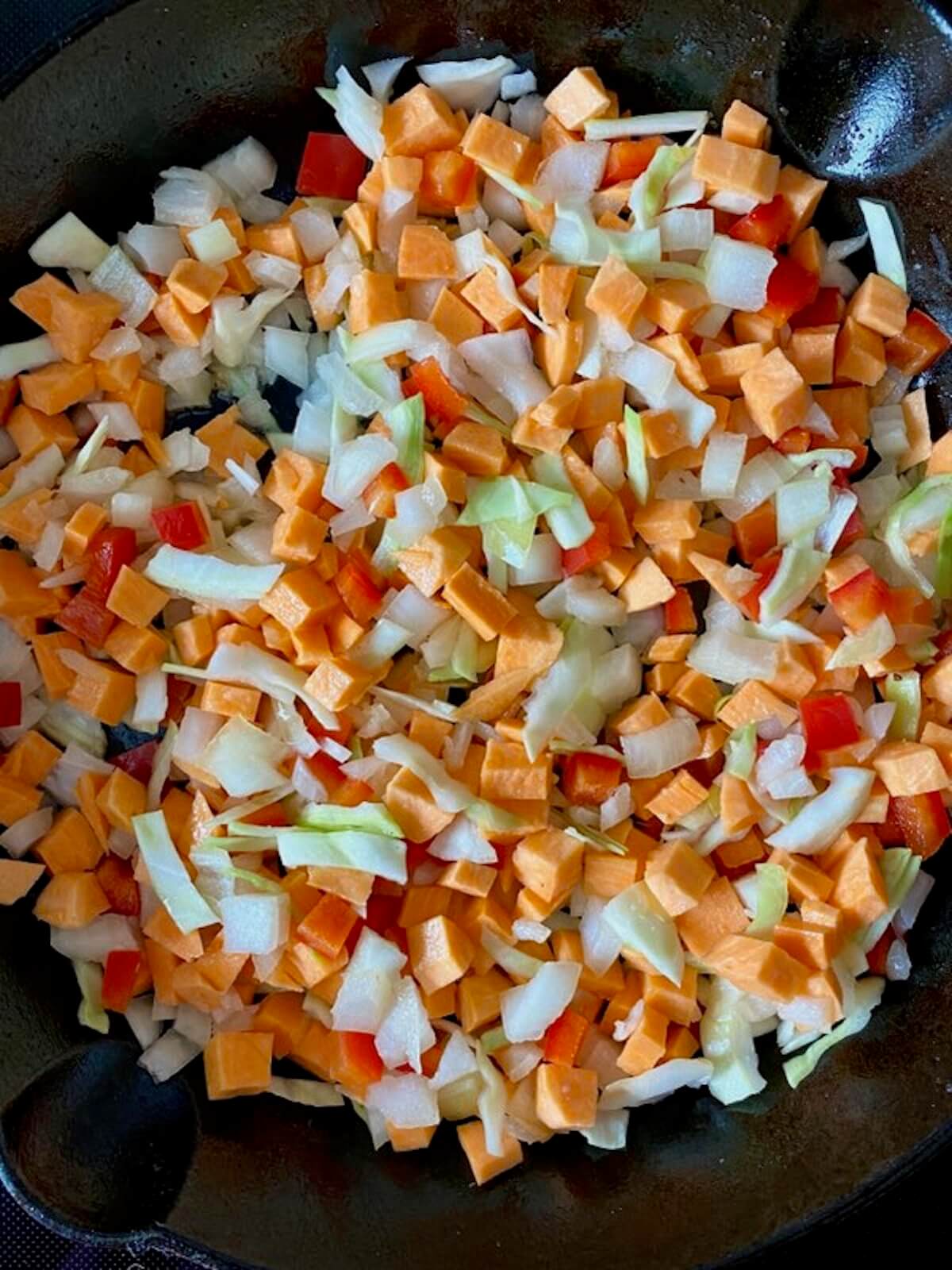 Diced sweet potato, red bell pepper, cabbage, and onion sautéing in a cast iron skillet.