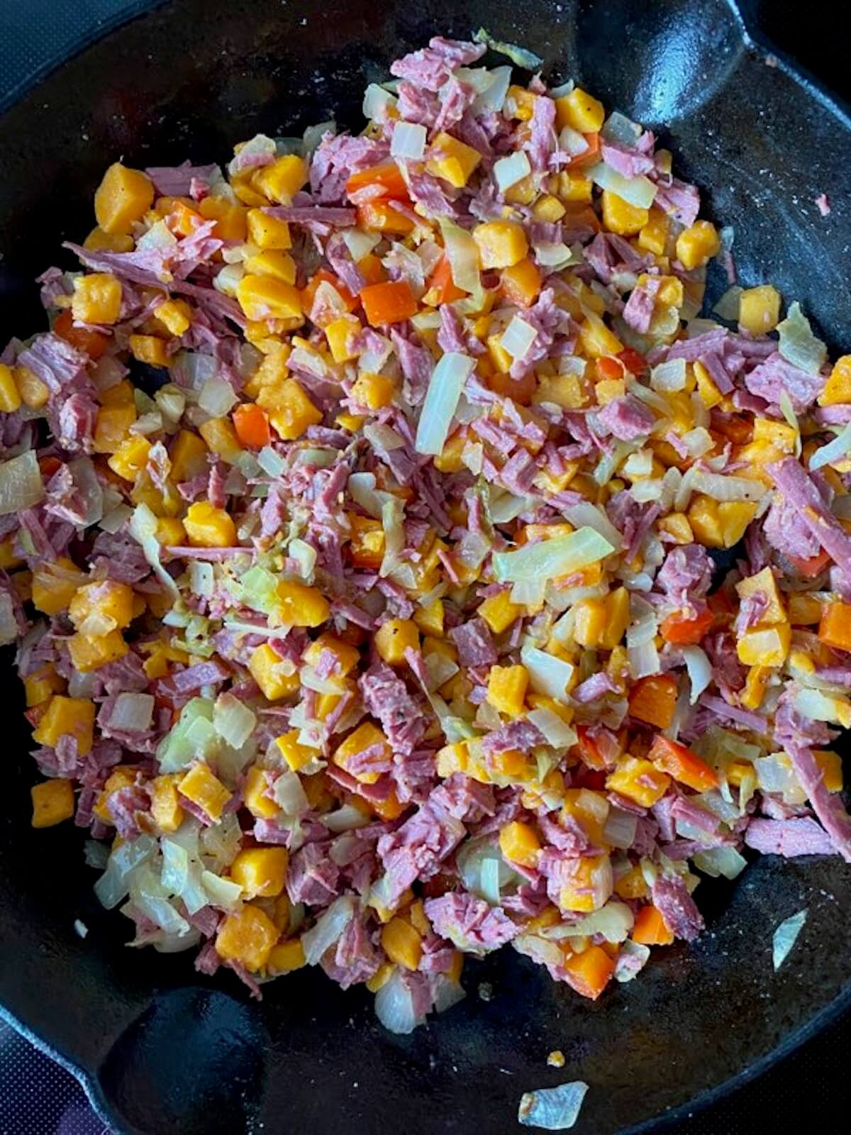 Sweet potato corned beef hash cooking in a cast iron skillet.