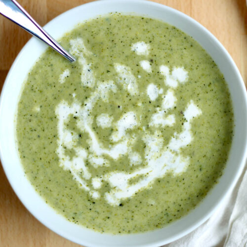 A bowl of creamy broccoli asparagus soup drizzled with cream.