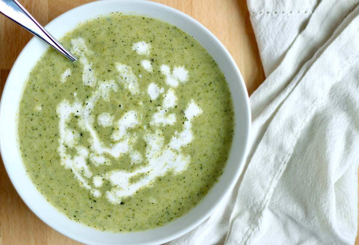 A bowl of broccoli asparagus soup drizzled with cream.