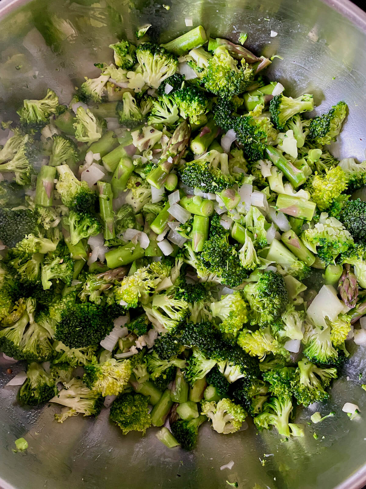 Broccoli, asparagus, onion, and garlic sautéing in a stainless steel stockpot.