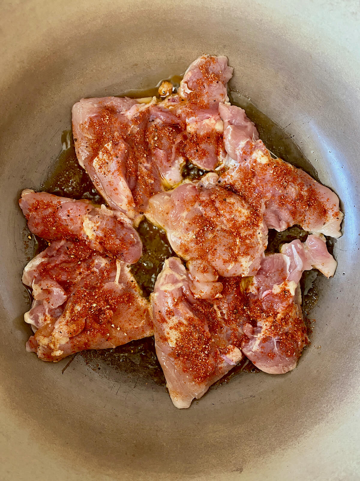 Seasoned chicken thighs searing in a cast iron pot.