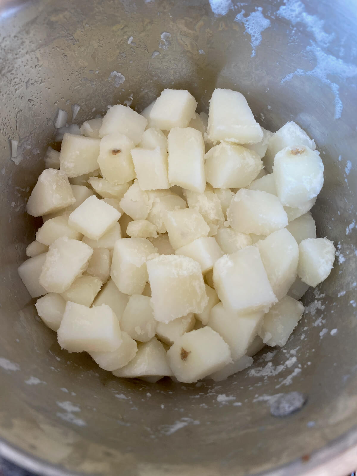 Cooked diced potatoes in a stainless steel pot.