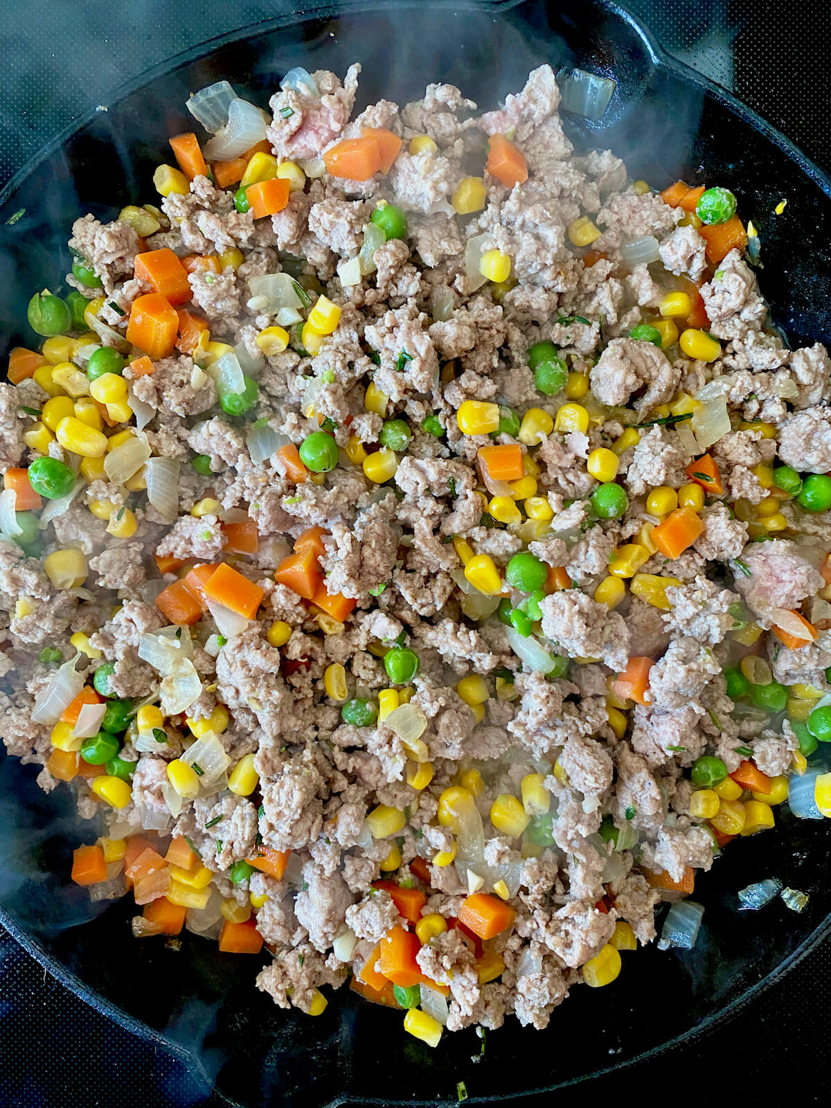 Ground turkey and vegetables being cooked together in a cast iron skillet.