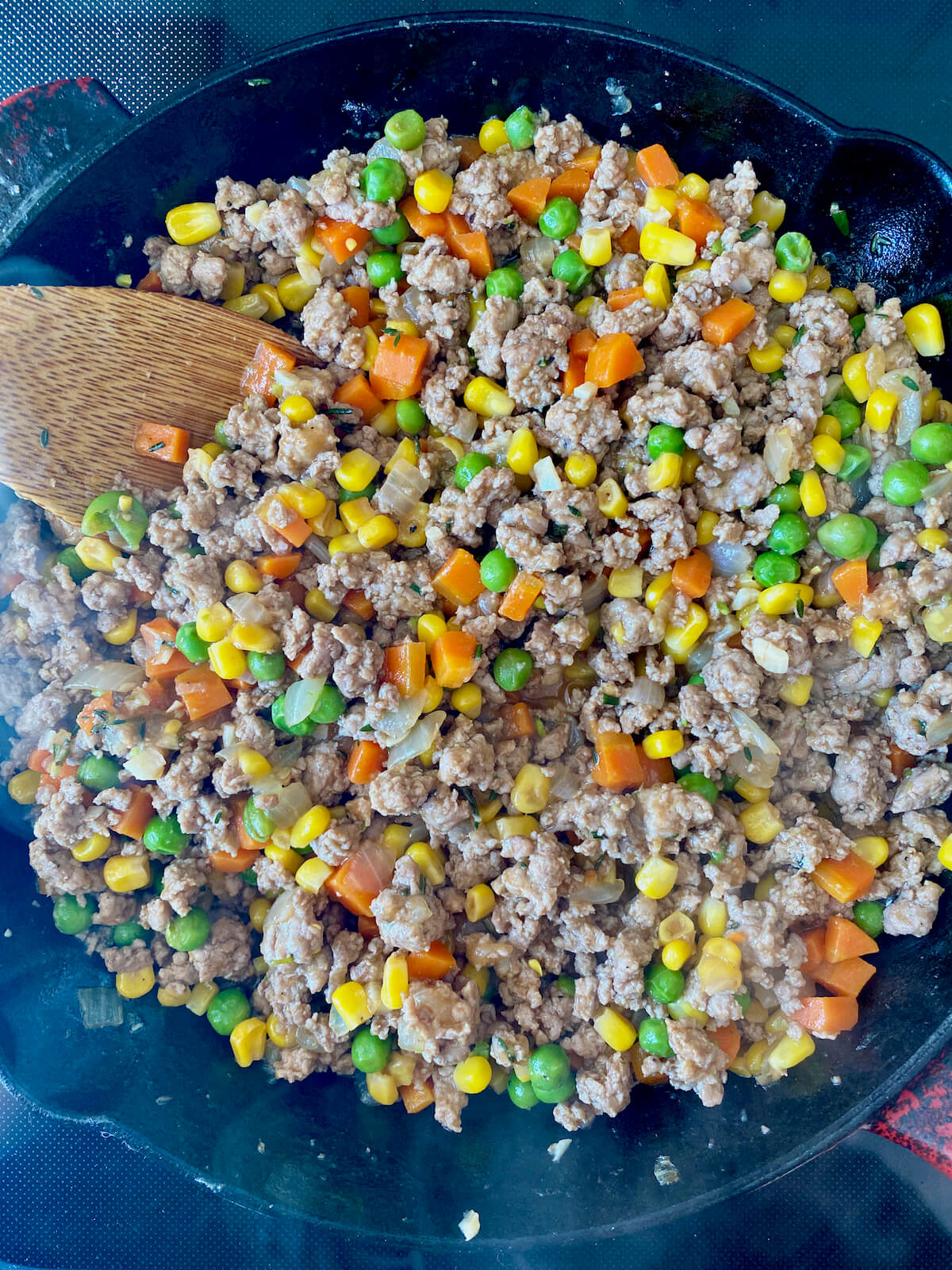 The finished ground turkey shepherd's pie filling in a cast iron skillet. There is a wooden spoon sticking out of the skillet to the left.