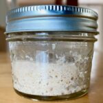 A bubbly, active sourdough starter in a small glass jar.