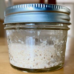 A bubbly, active sourdough starter in a small glass jar.