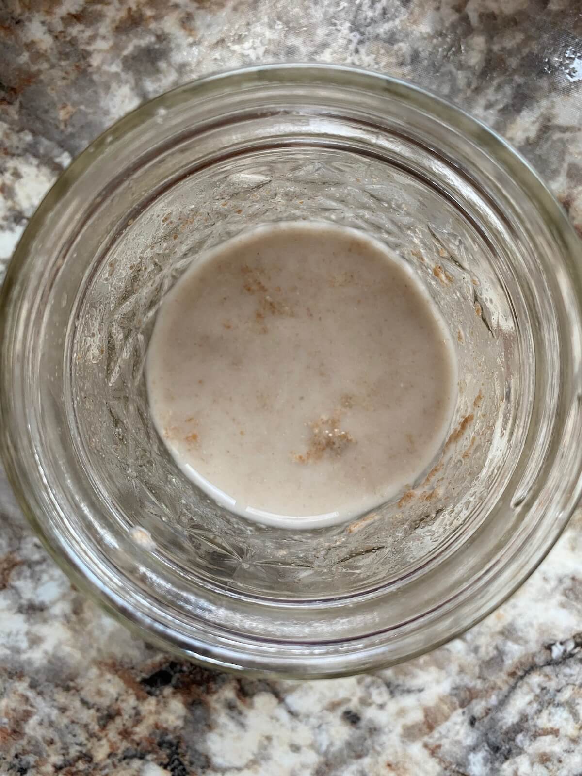 Sourdough starter mixed with warm water in a small glass jar.