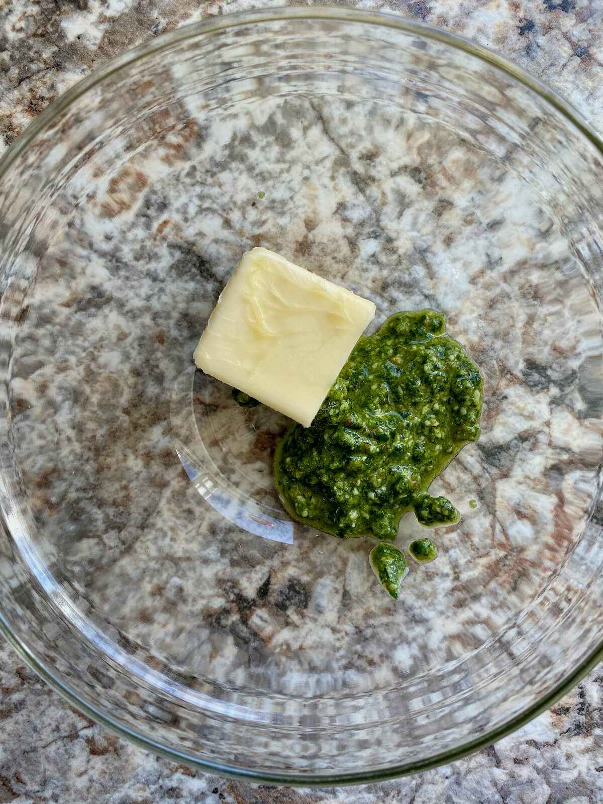 Butter and pesto in a glass mixing bowl.