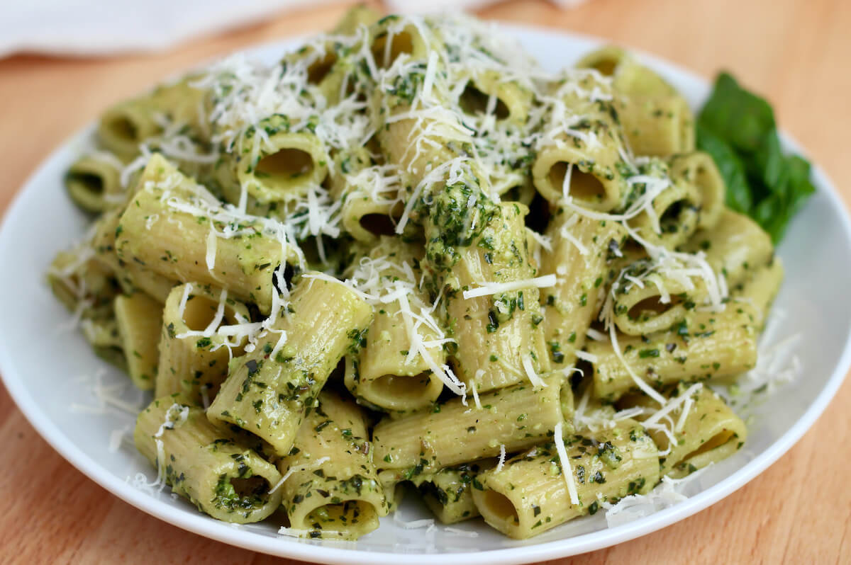 Rigatoni with pesto on a white plate topped with grated parmesan cheese.