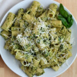 A plate of pesto rigatoni garnished with parmesan cheese and basil.