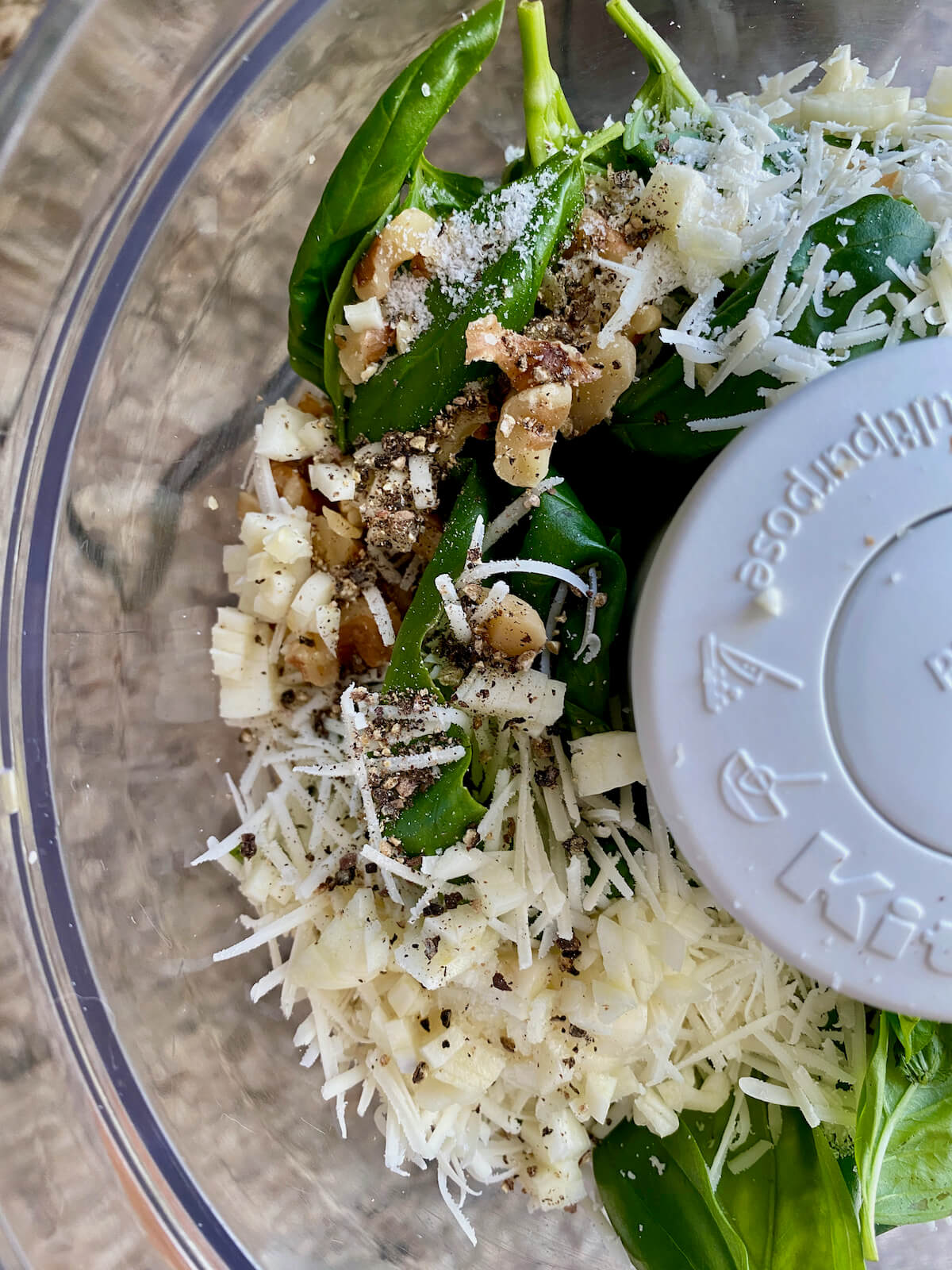 Basil leaves, grated parmesan, chopped walnuts, and garlic in the bowl of a food processor.