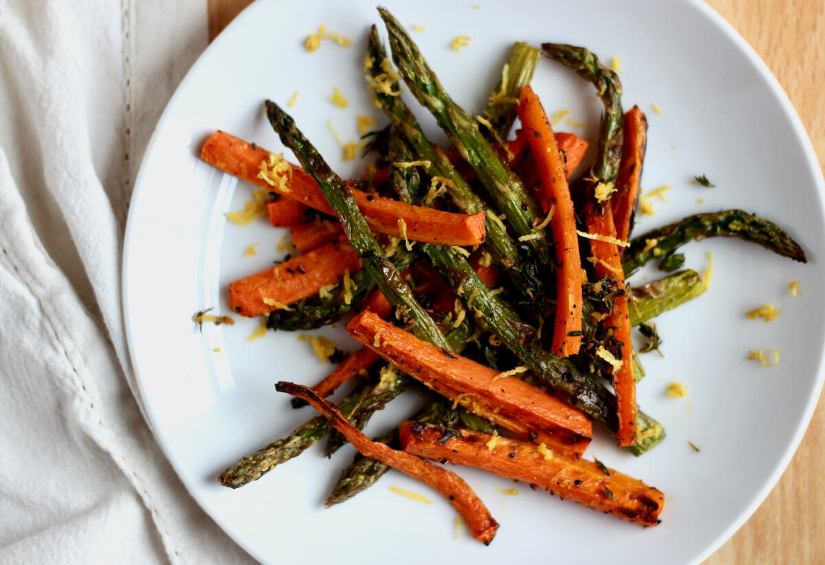 A small white plate of roasted carrots and asparagus garnished with lemon zest.