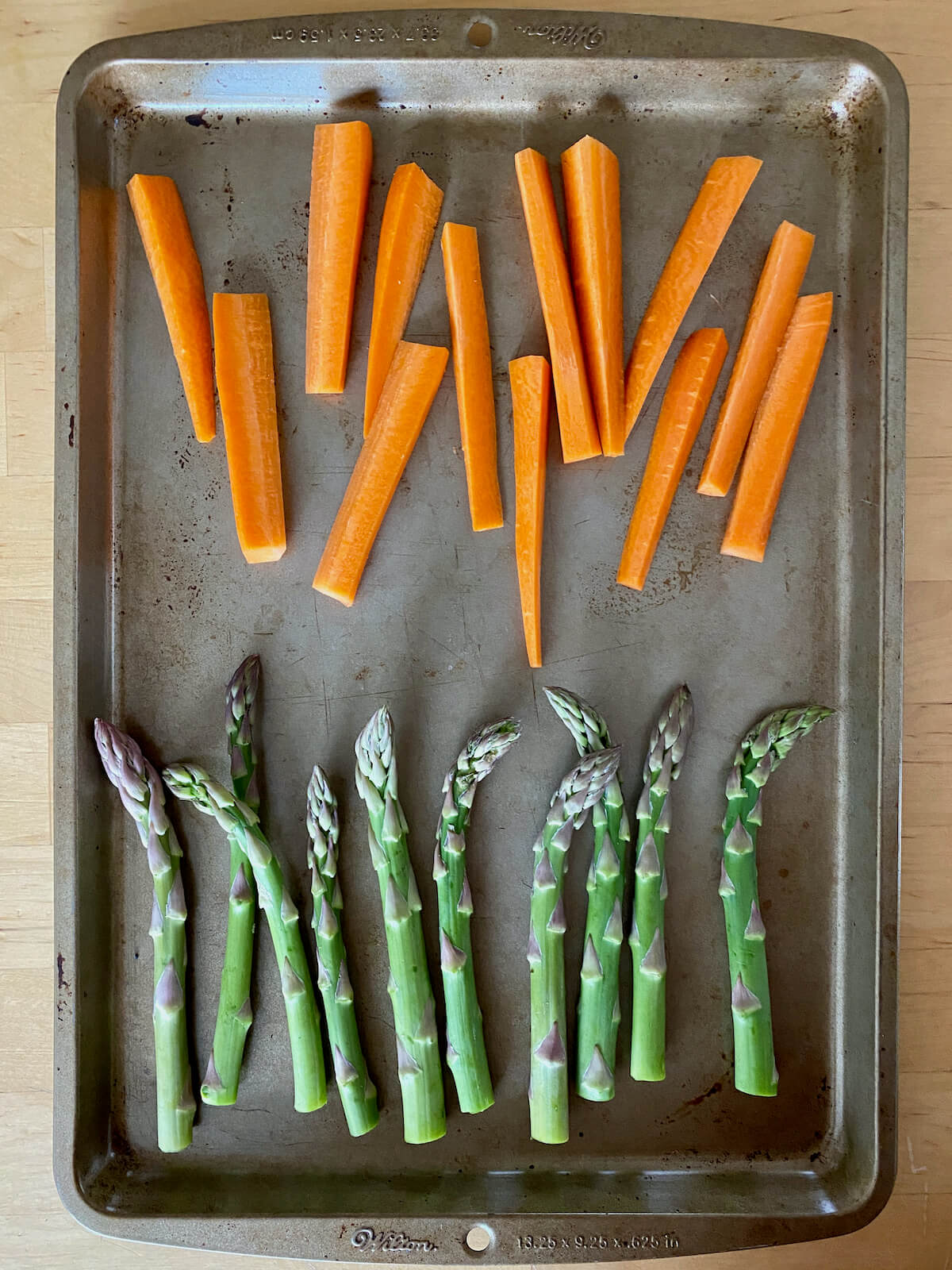 A rimmed baking sheet with trimmed asparagus and carrot sticks on it.