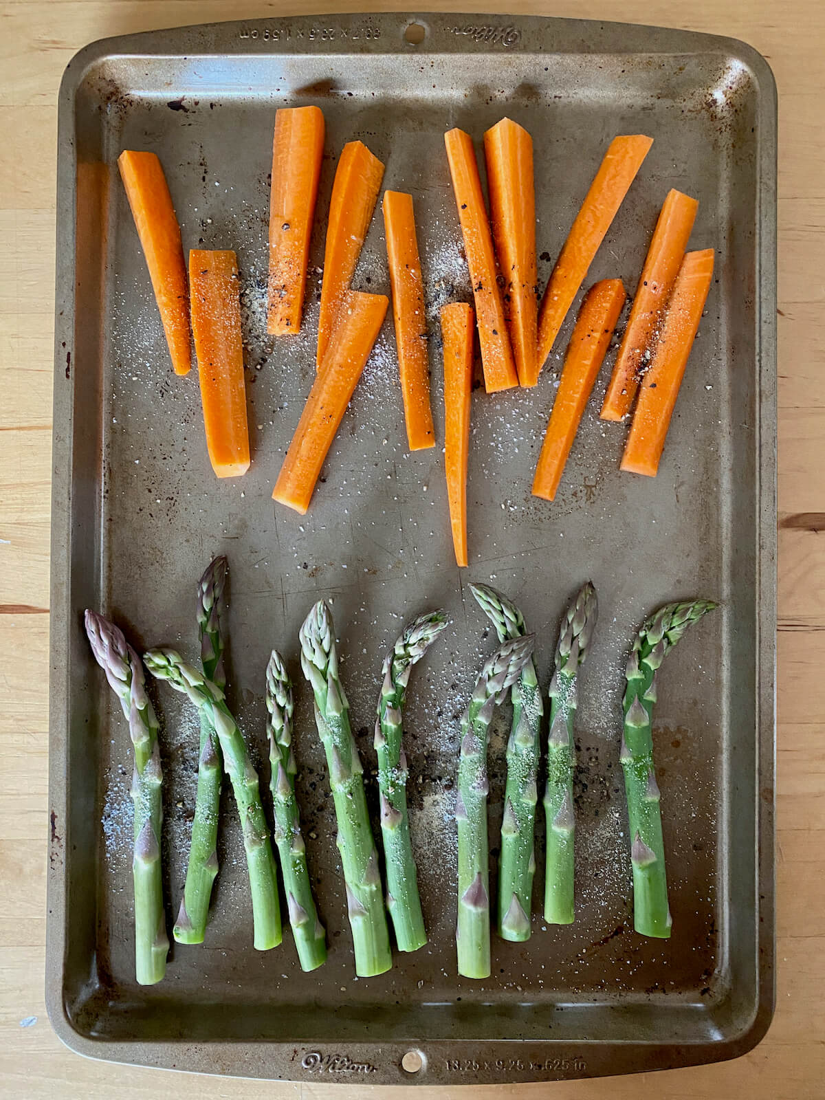 Seasoned asparagus and carrots on a rimmed baking sheet.